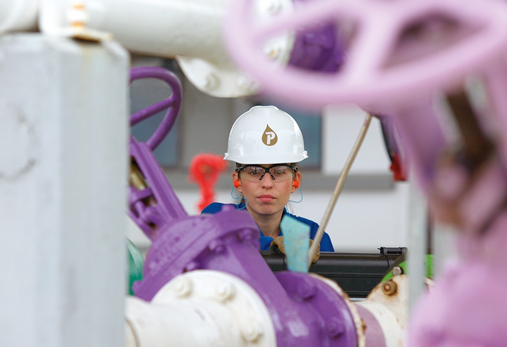 A Petrofac engineer working, surrounded by pipes. 